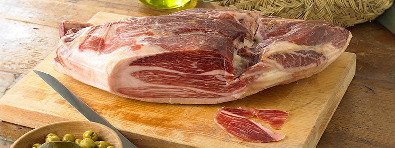 Photo of a boneless jamon serrano surrounded by fresh herbs and guindilla peppers