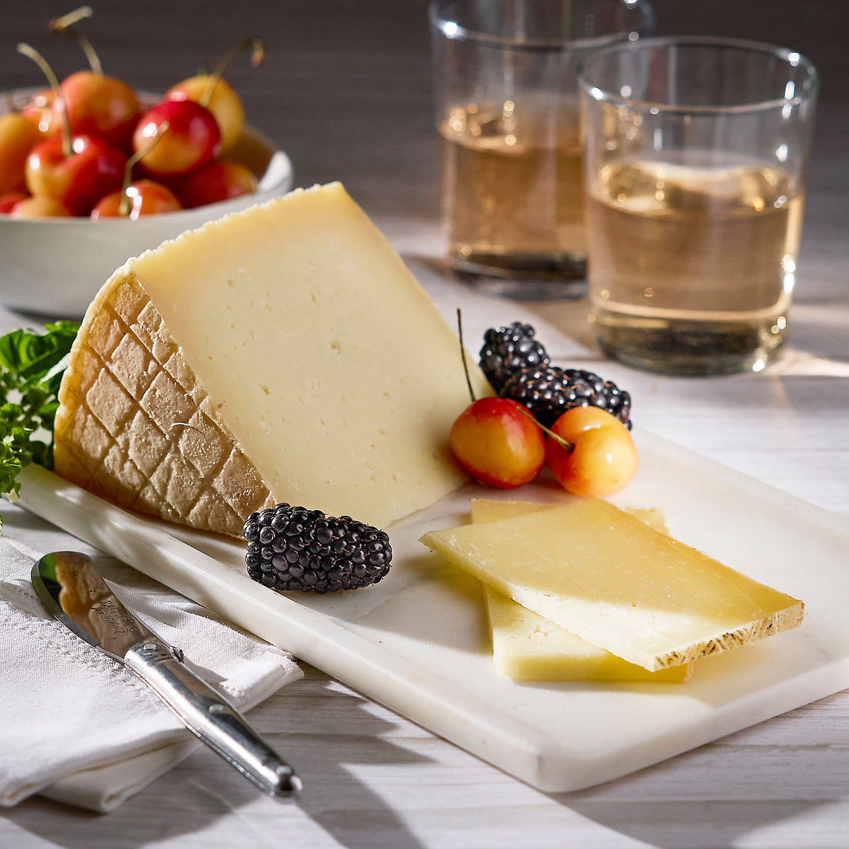 Photo of a wedge of Zamorano Sheep's Milk Cheese on a board with fruit