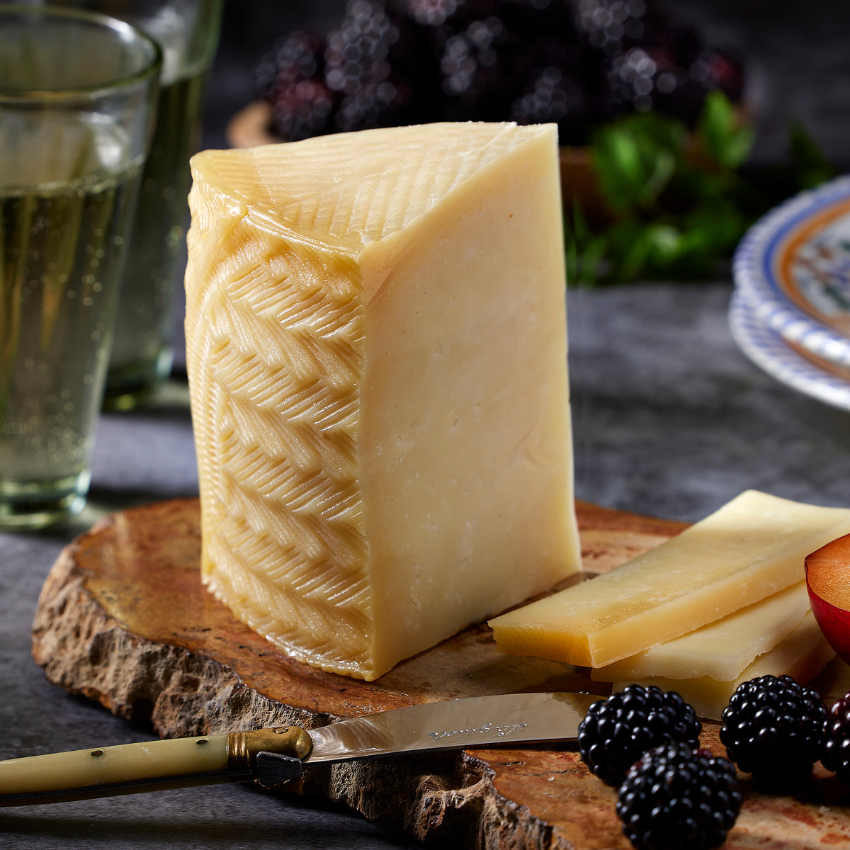 Photo of  a wedge of Young Manchego Cheese by Villajos on a wooden board with fruit